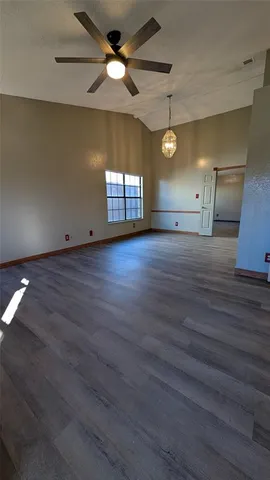 an empty room with wooden floor chandelier fan and windows