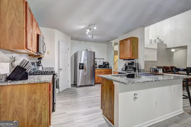 a kitchen with stainless steel appliances granite countertop a refrigerator a sink dishwasher a stove with wooden cabinets and floor