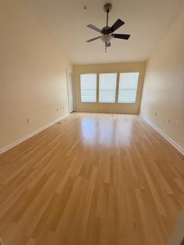 an empty room with wooden floor ceiling fan and windows