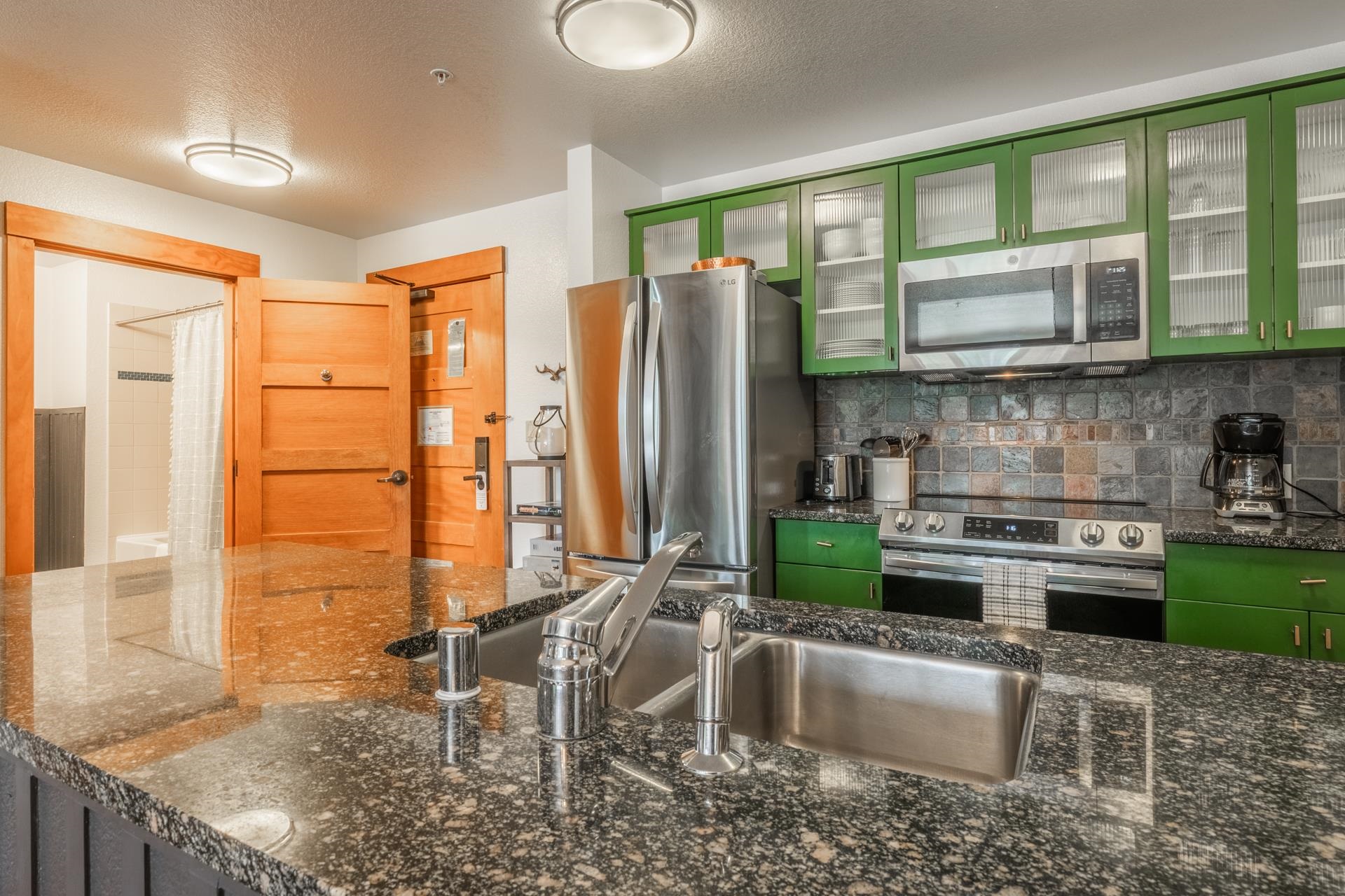 6201 Minaret Road, Unit 2221 Mammoth Lakes, CA 93546 - Photo 11 of 32 Kitchen featuring a stainless steel undermount sink, granite countertops, green cabinetry, stainless steel appliances, and a tiled backsplash