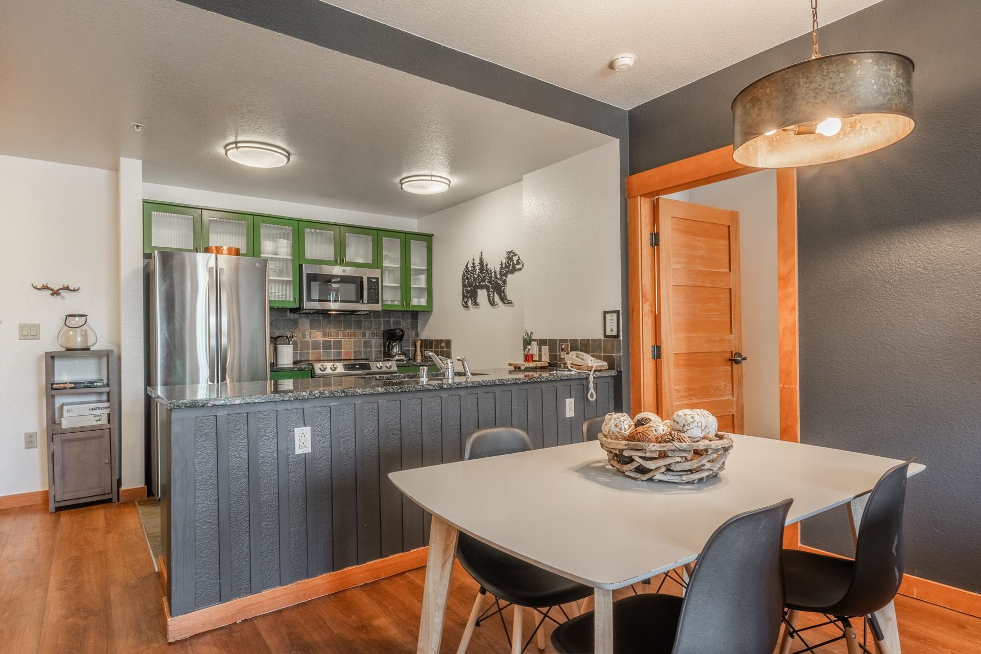 6201 Minaret Road, Unit 2221 Mammoth Lakes, CA 93546 - Photo 12 of 32 Open-concept kitchen and dining area featuring wood-finish flooring, green upper cabinetry, stainless steel appliances, a dark stone-finish countertop, and a textured accent wall