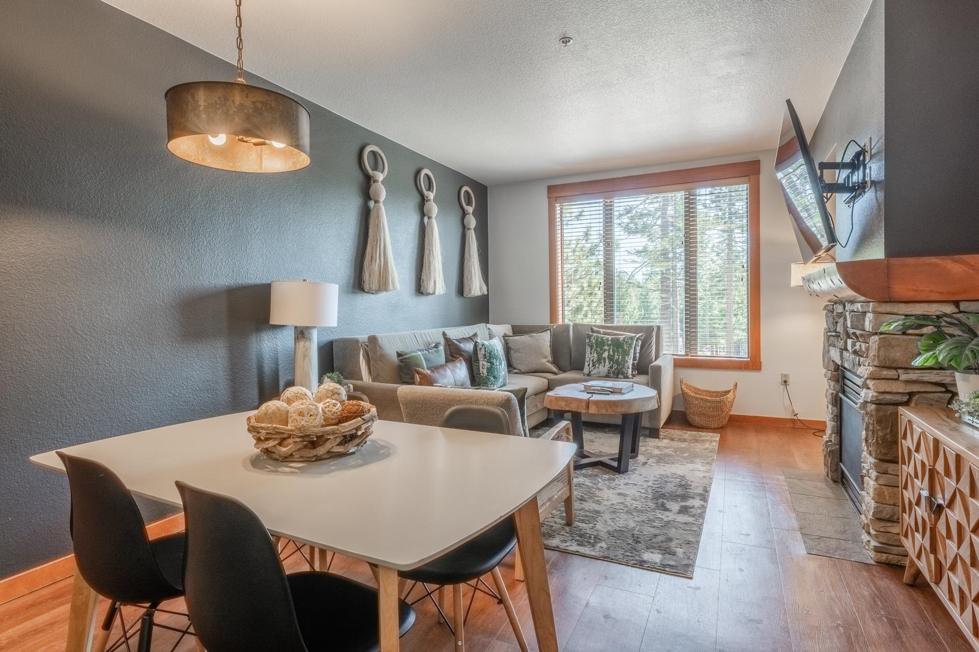 6201 Minaret Road, Unit 2221 Mammoth Lakes, CA 93546 - Photo 15 of 32 Open-concept living area featuring a stone fireplace with a wood mantle, wood-finish flooring, and a large picture window with wood trim