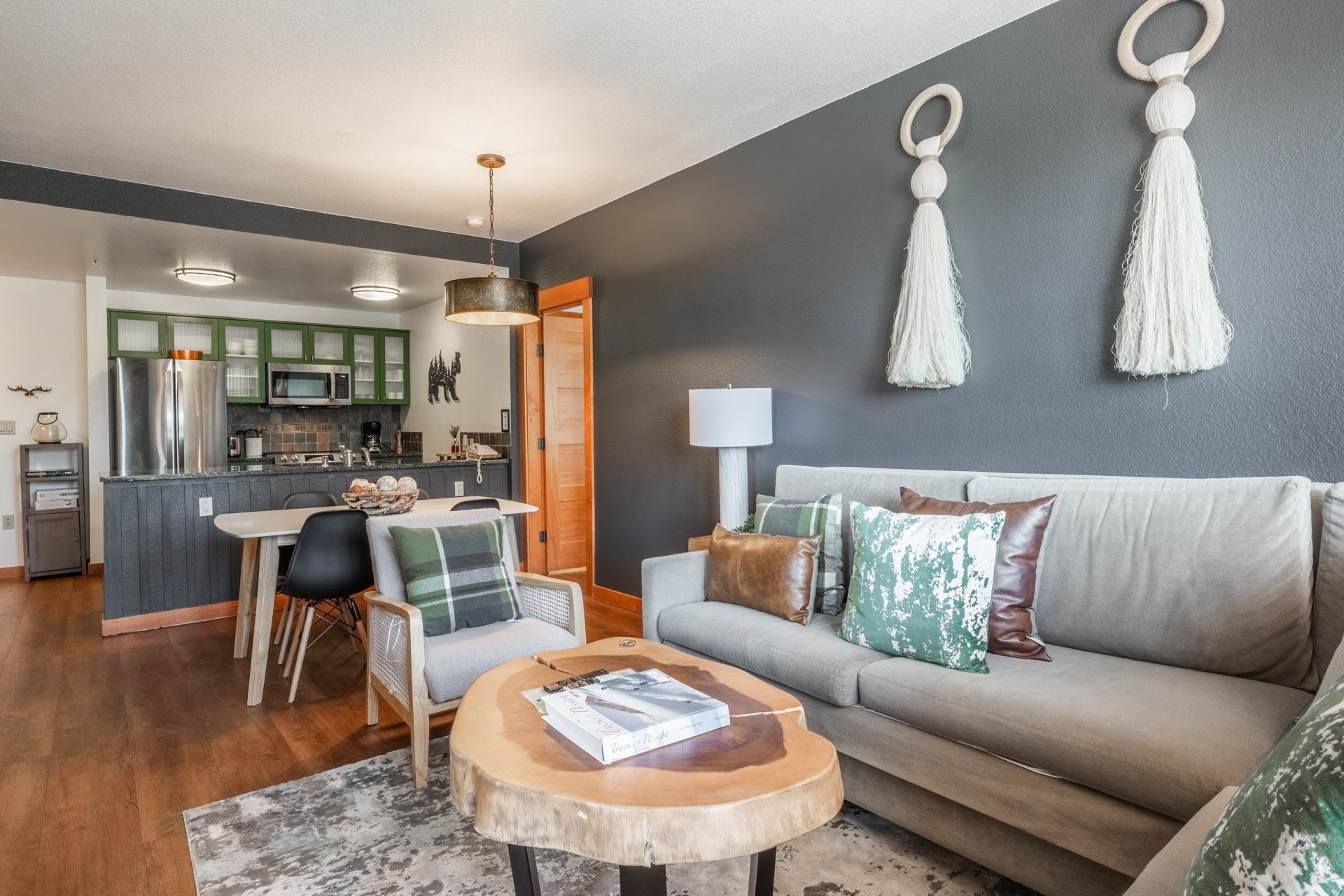 6201 Minaret Road, Unit 2221 Mammoth Lakes, CA 93546 - Photo 17 of 32 Open-concept living space featuring wood-finish flooring, a dark accent wall, and a kitchen with olive green cabinetry, stainless steel appliances, and a breakfast bar