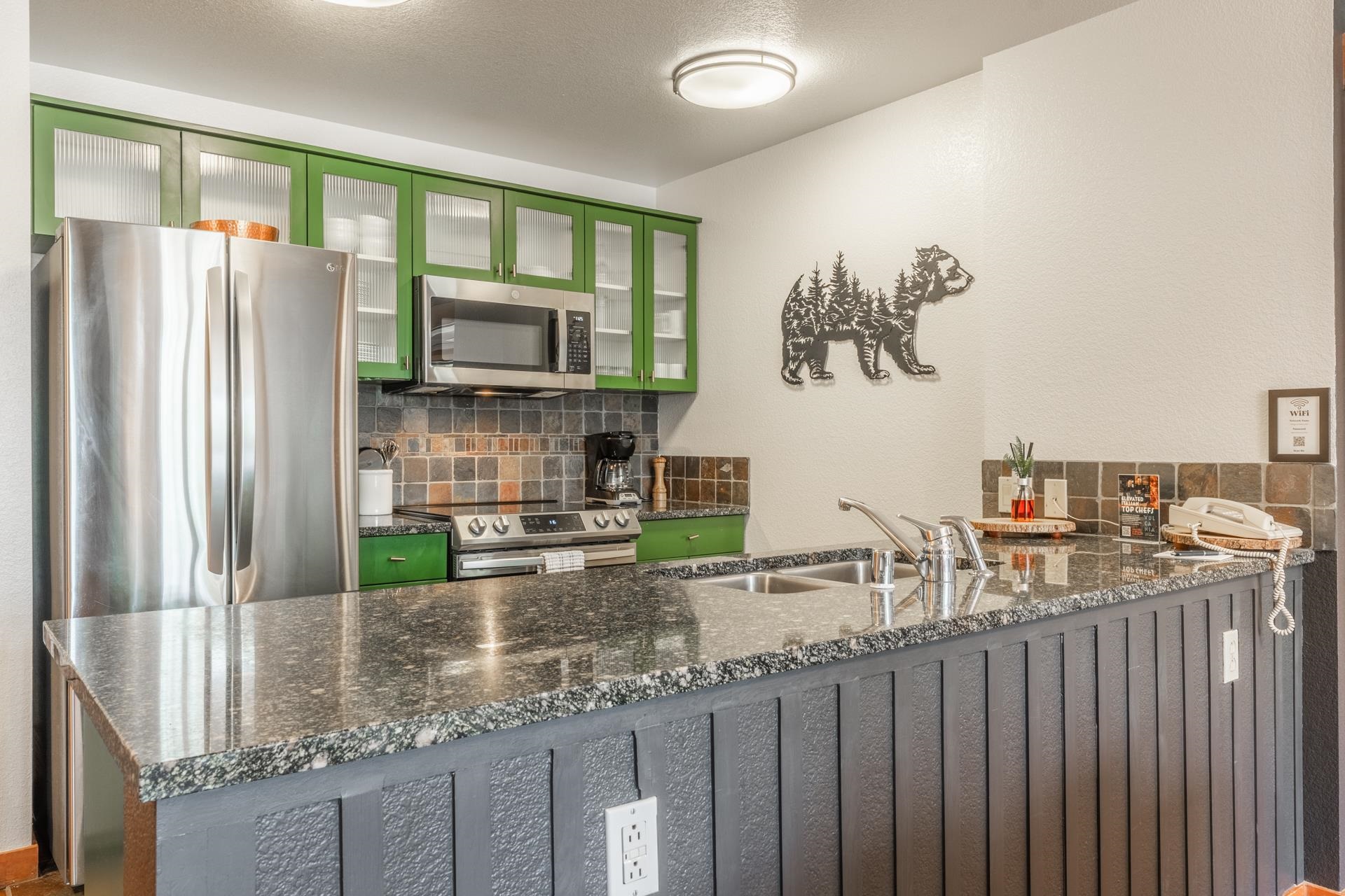 6201 Minaret Road, Unit 2221 Mammoth Lakes, CA 93546 - Photo 9 of 32 Kitchen featuring granite countertops, stainless steel appliances, vibrant green upper cabinetry with glass inserts, a tiled backsplash, and a double basin sink