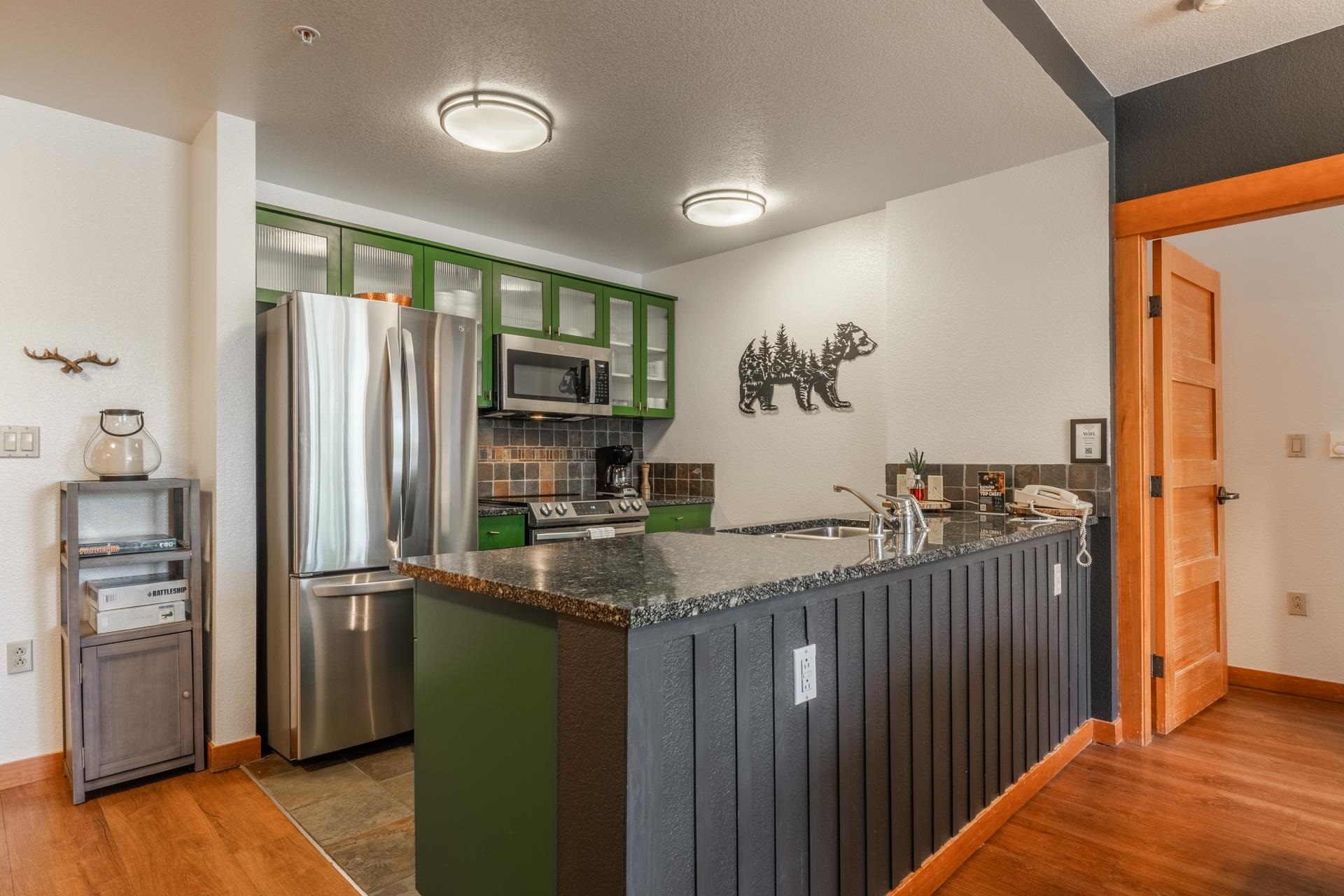 6201 Minaret Road, Unit 2221 Mammoth Lakes, CA 93546 - Photo 10 of 32 Kitchen featuring green cabinetry, stainless steel appliances, a dark granite countertop, and a breakfast bar with beadboard paneling