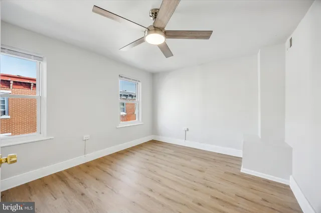 an empty room with wooden floor fan and windows