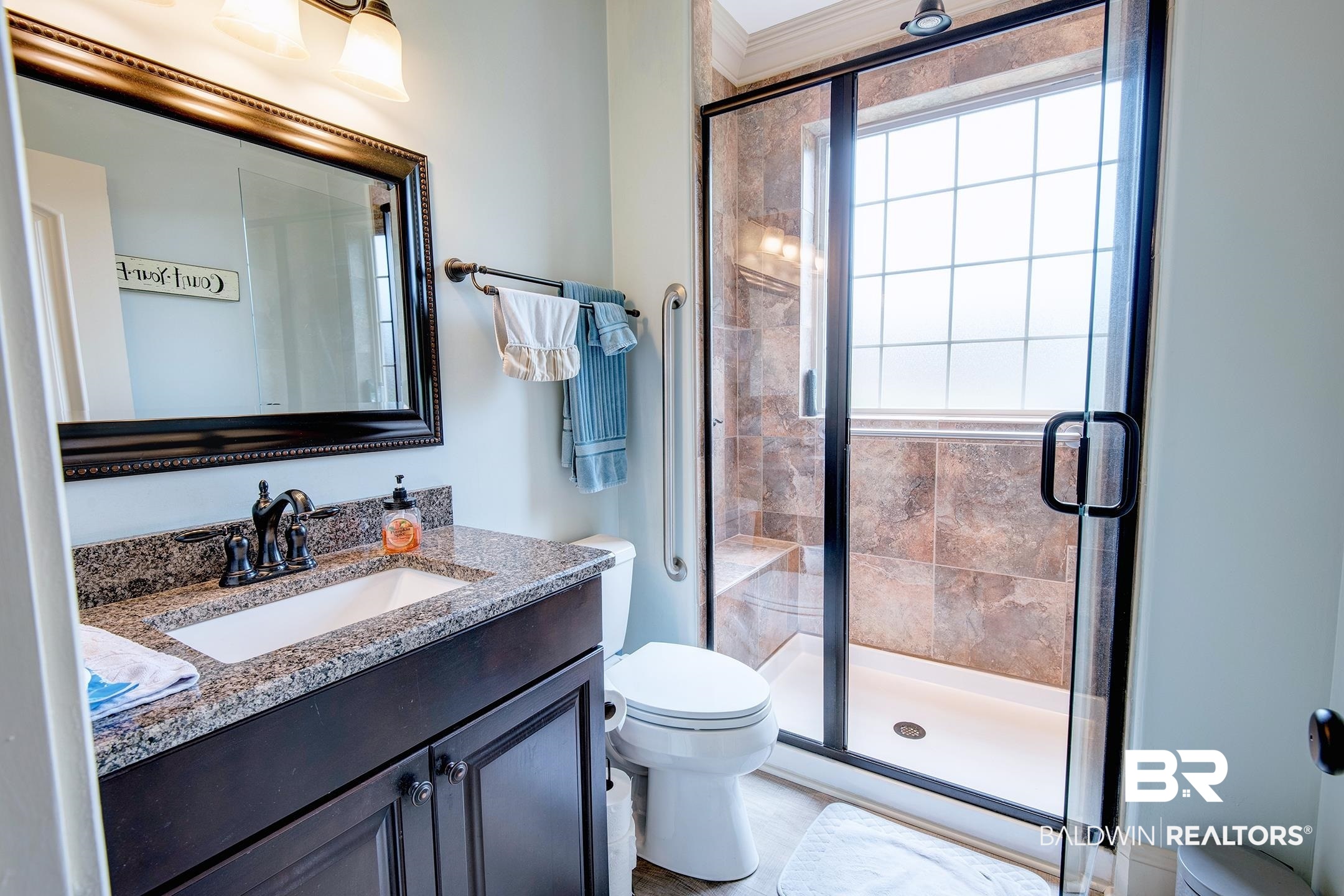 9357 Lakeview Drive Foley, AL 36535 - Photo 51 of 68 Spacious bathroom featuring a glass-enclosed shower with tile surround and integrated bench, a window with grid pattern, and a vanity with granite countertop and dark wood-finish cabinetry