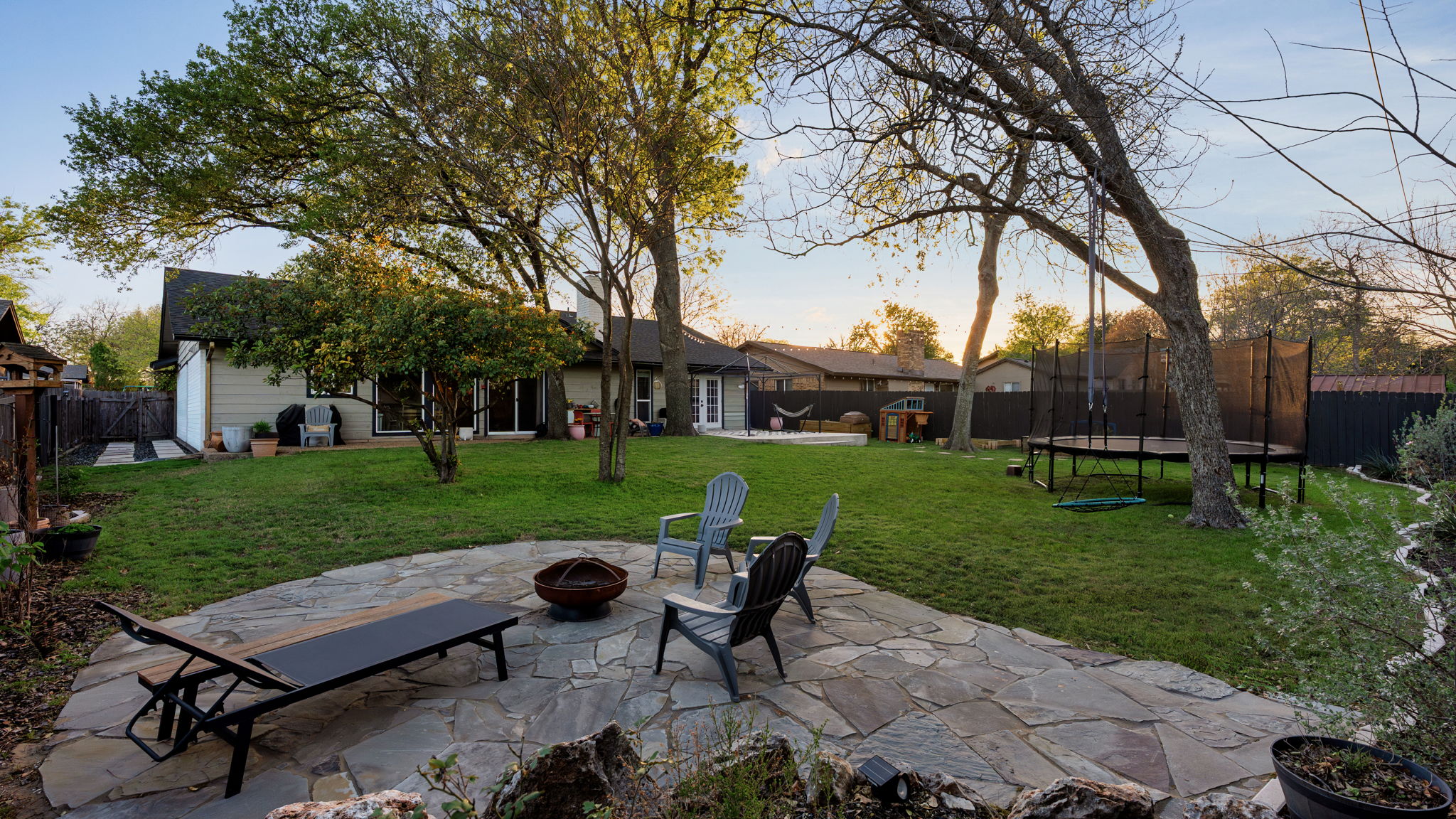 1602 Thornridge Road Austin, TX 78758 - Photo 33 of 39 Patio terrace at dusk featuring a patio, a fenced backyard, a fire pit, and a trampoline