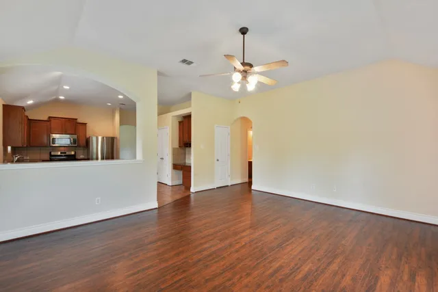 a view of an empty room with wooden floor and a kitchen