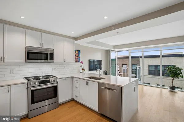 a kitchen with stainless steel appliances granite countertop a stove a sink a refrigerator white cabinets and wooden floor