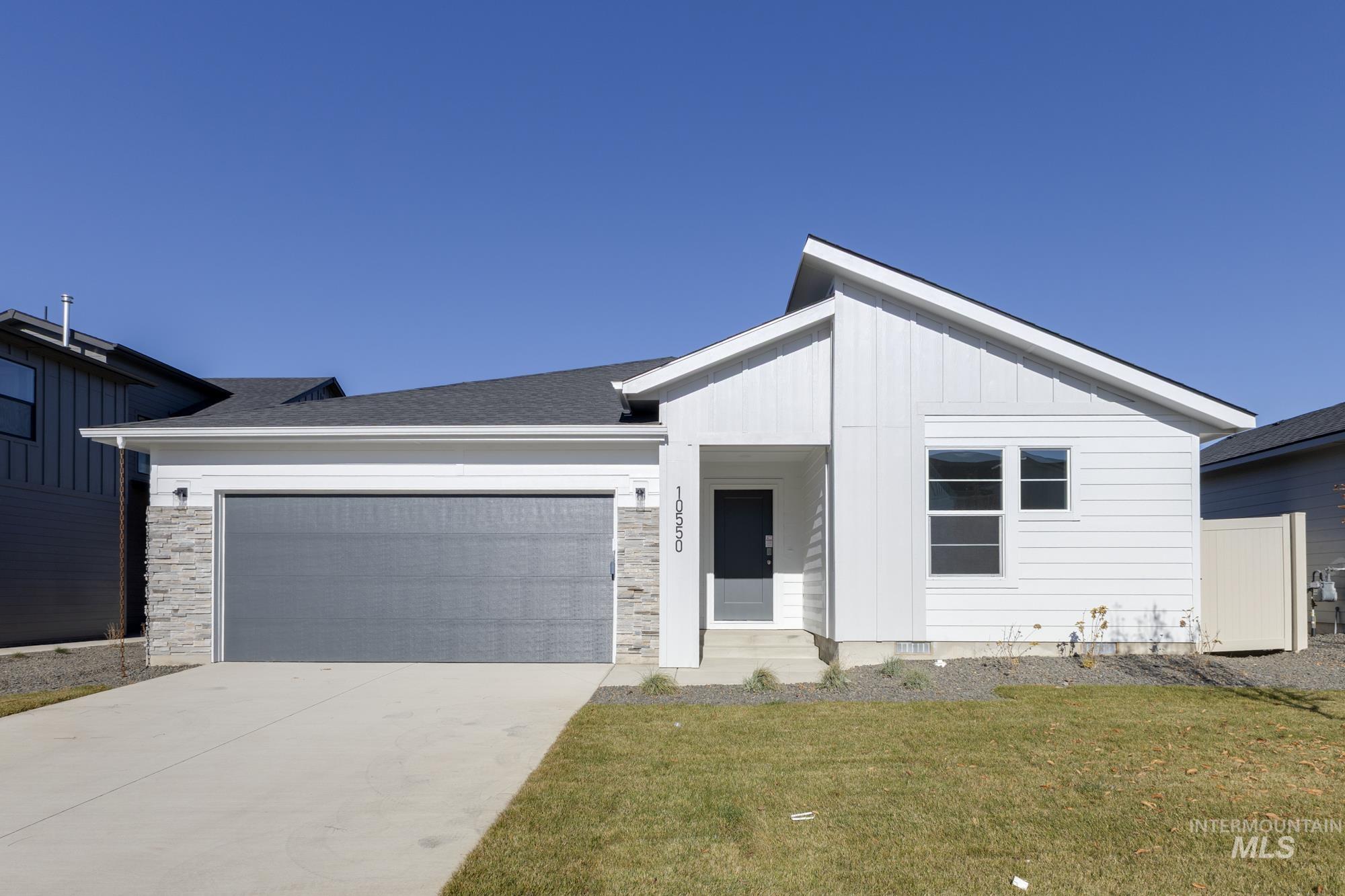 View of front of property with an attached garage, concrete driveway, board and batten siding, a front yard, and stone siding