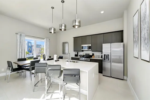 a room with stainless steel appliances kitchen island granite countertop a refrigerator a stove top oven a sink dishwasher and a dining table with wooden floor