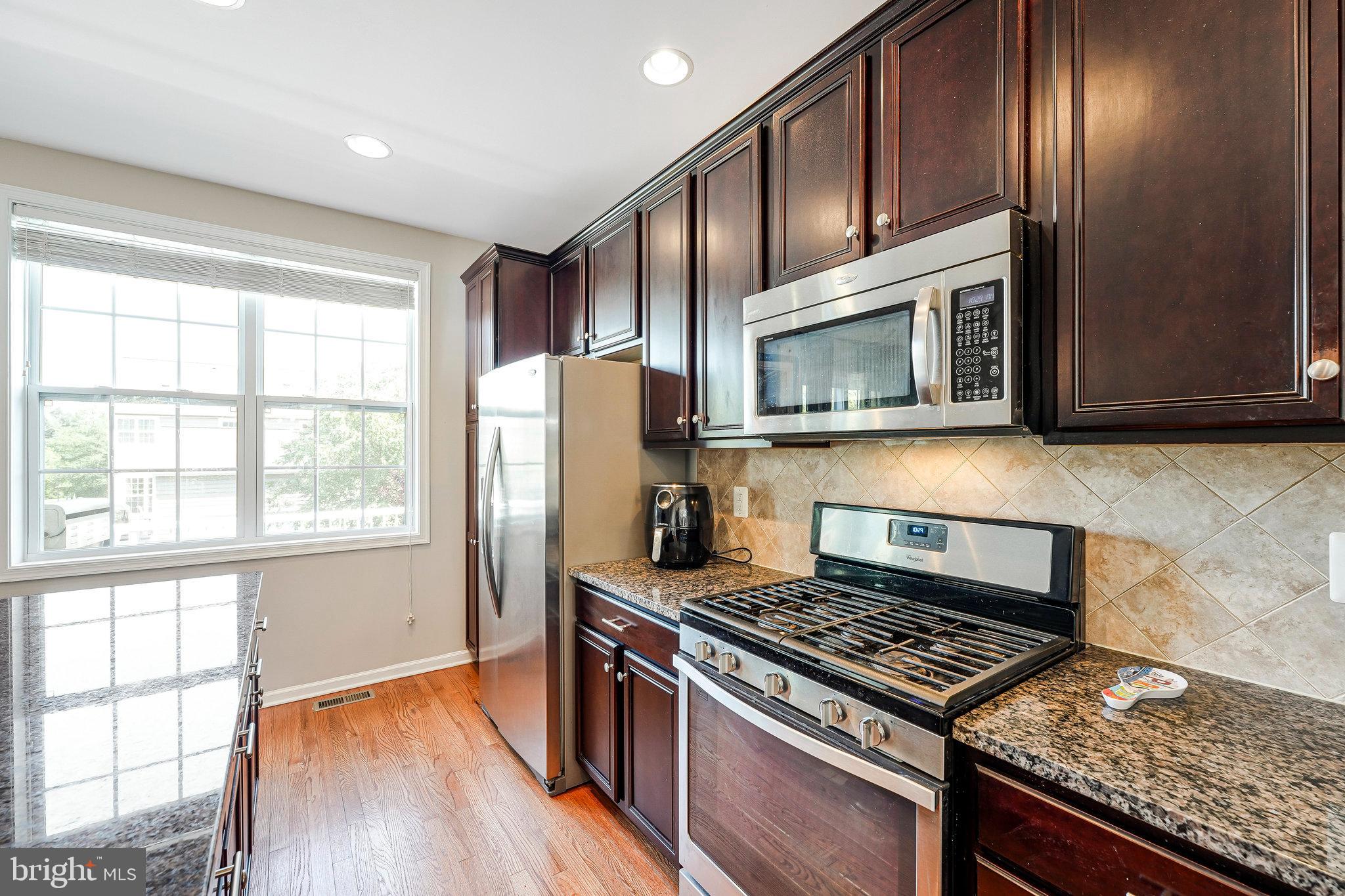 23073 Weybridge Square Broadlands, VA 20148 - Photo 7 of 24 a kitchen with granite countertop wooden cabinets stainless steel appliances and a window