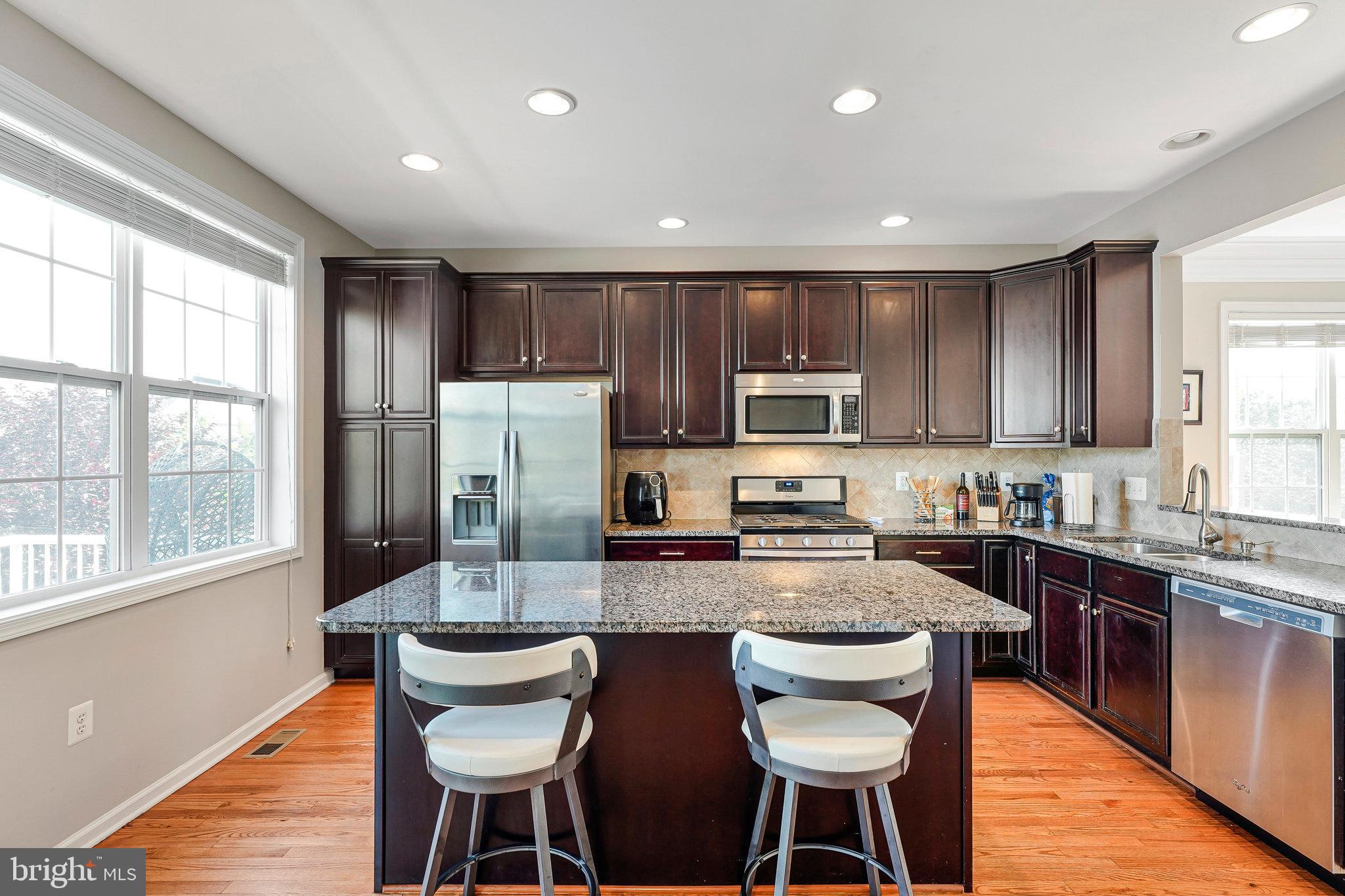 23073 Weybridge Square Broadlands, VA 20148 - Photo 10 of 24 a kitchen with granite countertop a dining table chairs wooden cabinets and stainless steel appliances
