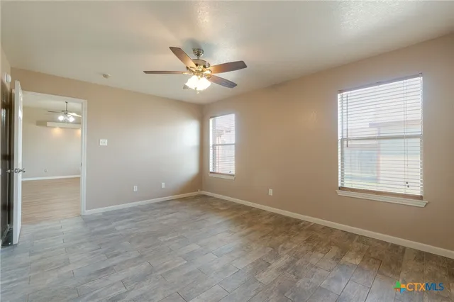 an empty room with wooden floor fan and windows