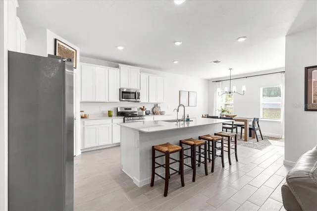 a kitchen with stainless steel appliances kitchen island granite countertop a stove top oven a sink a refrigerator white cabinets and wooden floor