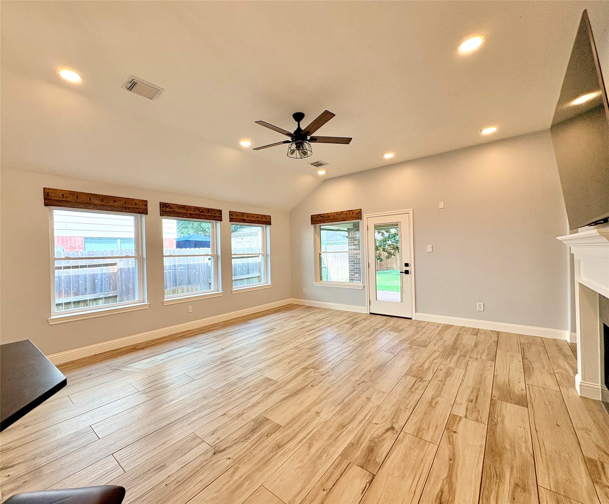 15410 Redbud Berry Way Cypress, TX 77433 - Photo 15 of 49 Spacious, well-lit living room with vaulted ceiling, large windows, and wood-look flooring. Features a ceiling fan and a door leading to the backyard, perfect for entertaining or relaxing.