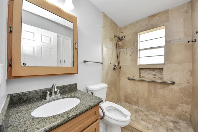 a bathroom with a granite countertop sink toilet a mirror and shower