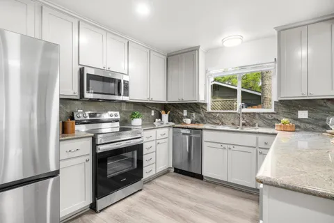 a kitchen with granite countertop white cabinets stainless steel appliances a sink and a window
