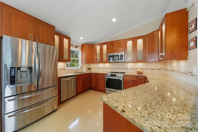 a kitchen with stainless steel appliances granite countertop a refrigerator a stove and a sink with wooden cabinets