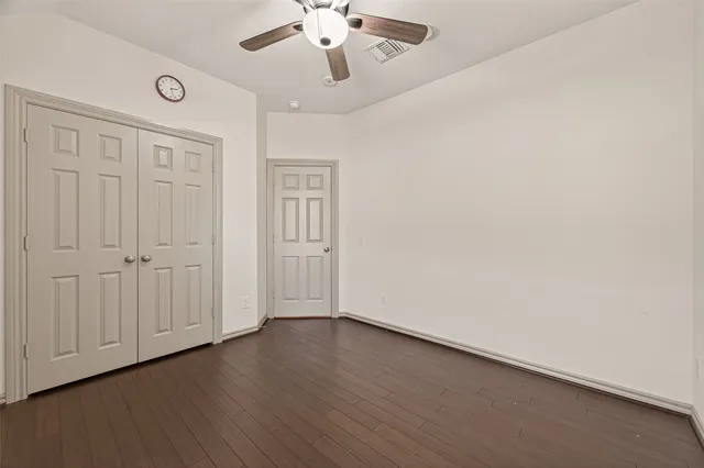 an empty room with wooden floor chandelier fan and windows