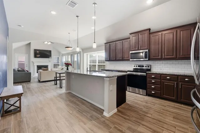 a kitchen with kitchen island granite countertop wooden floors wooden cabinets appliances and a window