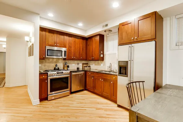 a kitchen with stainless steel appliances granite countertop a stove top oven a sink dishwasher a refrigerator and a microwave with wooden floor