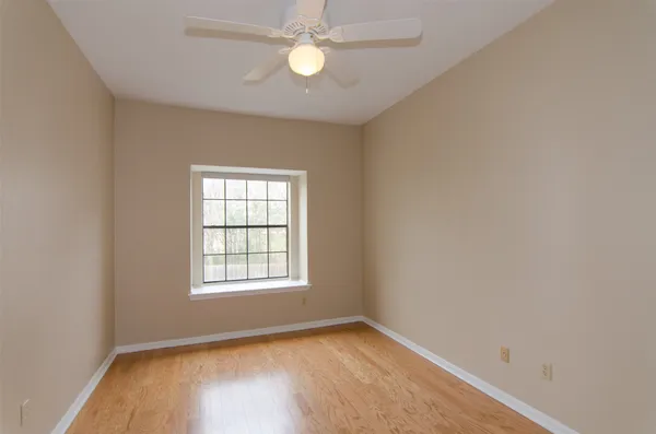 an empty room with wooden floor ceiling fan and windows