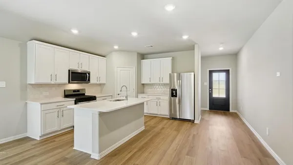 a kitchen with stainless steel appliances a stove top oven a refrigerator a sink and dishwasher with wooden floor