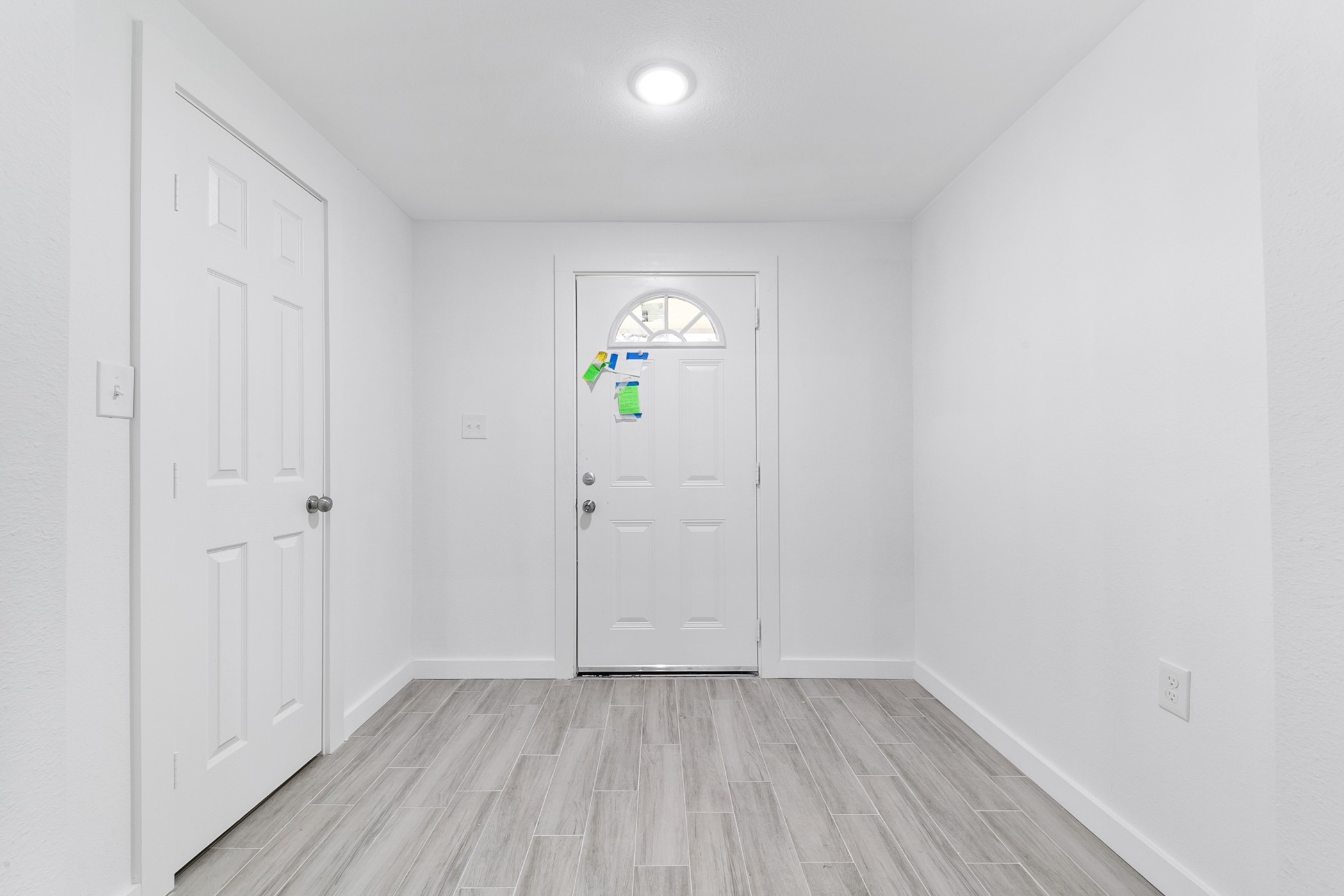 6811 McCullum Road Houston, TX 77489 - Photo 19 of 22 This photo shows a bright, minimalist entryway with white walls, a central light fixture, and light gray tile flooring. It features a standard front door with a small window and an adjacent interior door, offering a clean and welcoming atmosphere.