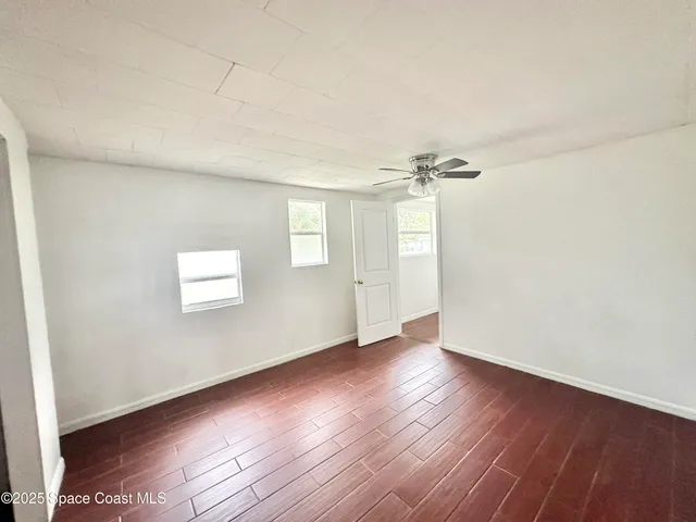 an empty room with wooden floor cabinet and windows