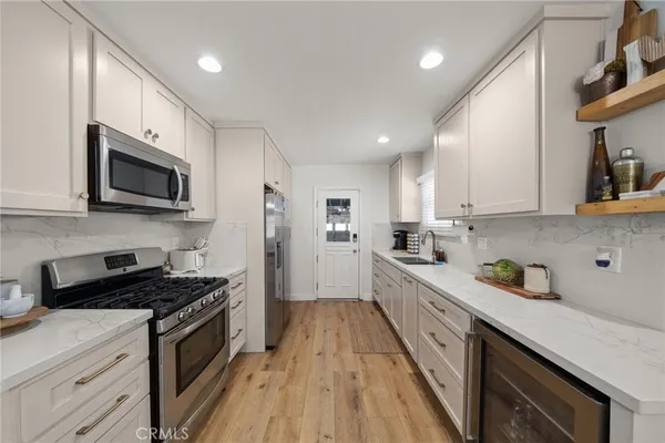 a kitchen with stainless steel appliances a sink dishwasher a stove top oven a refrigerator with wooden floor and cabinets