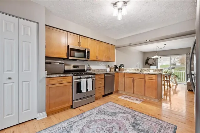 a kitchen with stainless steel appliances granite countertop a stove top oven a sink dishwasher a dining table and chairs with wooden floor