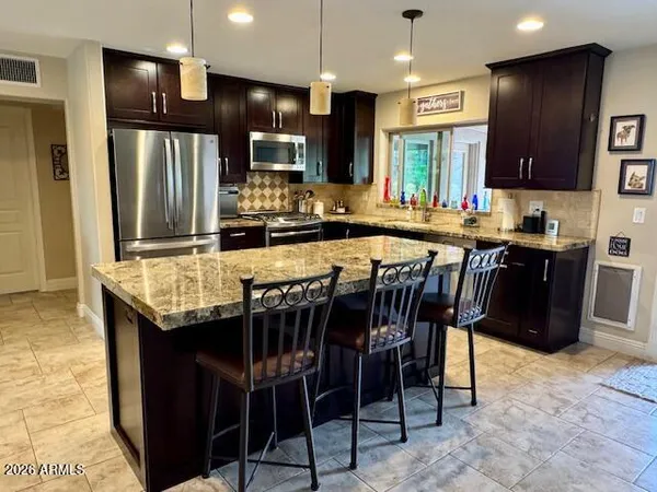 a kitchen with granite countertop a table chairs microwave and refrigerator
