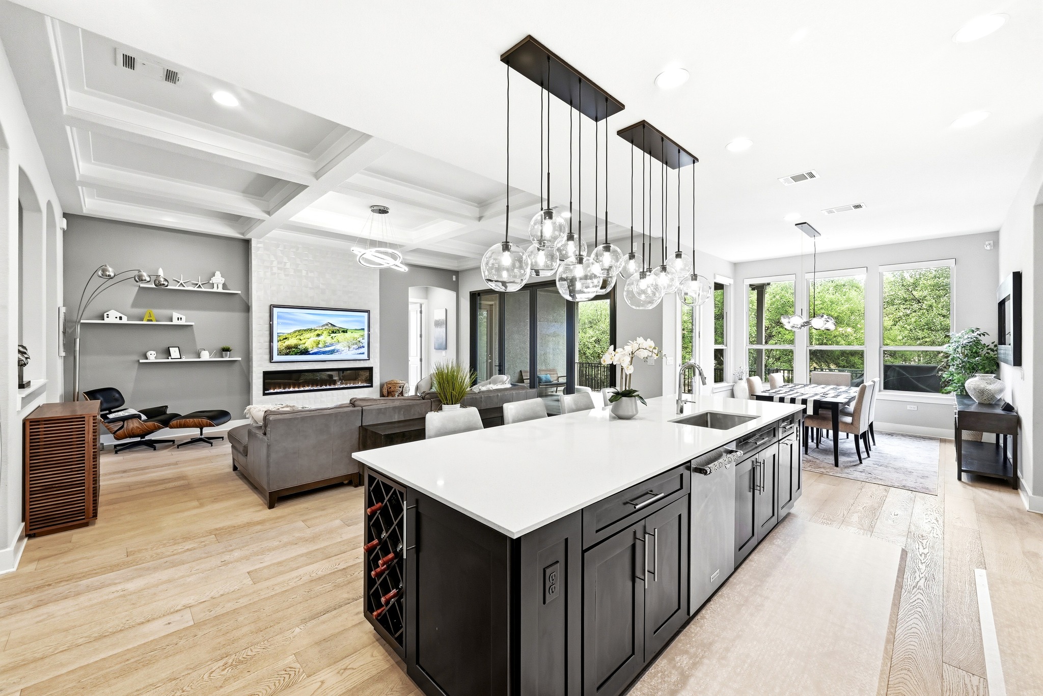 9008 Harper Rae Drive Austin, TX 78717 - Photo 14 of 39 Spacious open-concept living area featuring light wood-finish flooring, a kitchen island with built-in wine storage and pendant lighting, a modern fireplace, and large windows