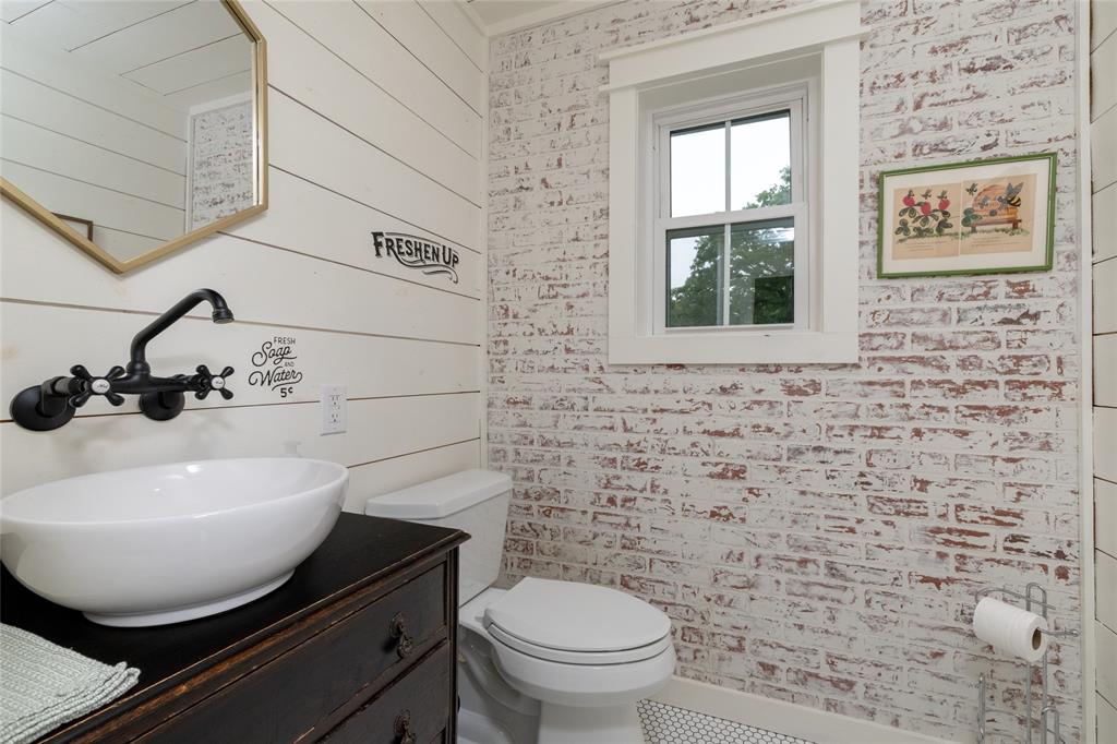 8948 David Fort Road Argyle, TX 76226 - Photo 26 of 39 Powder room featuring a vessel sink with a wall-mounted faucet, an antique-style vanity, ship-lap wall paneling, and a white-washed brick accent wall