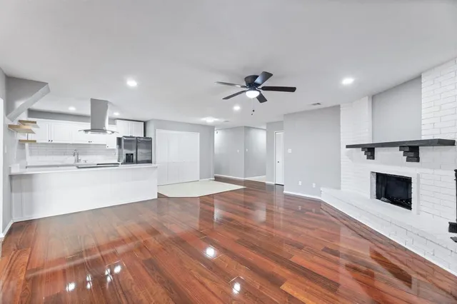 a view of an empty room and kitchen with fireplace wooden floor
