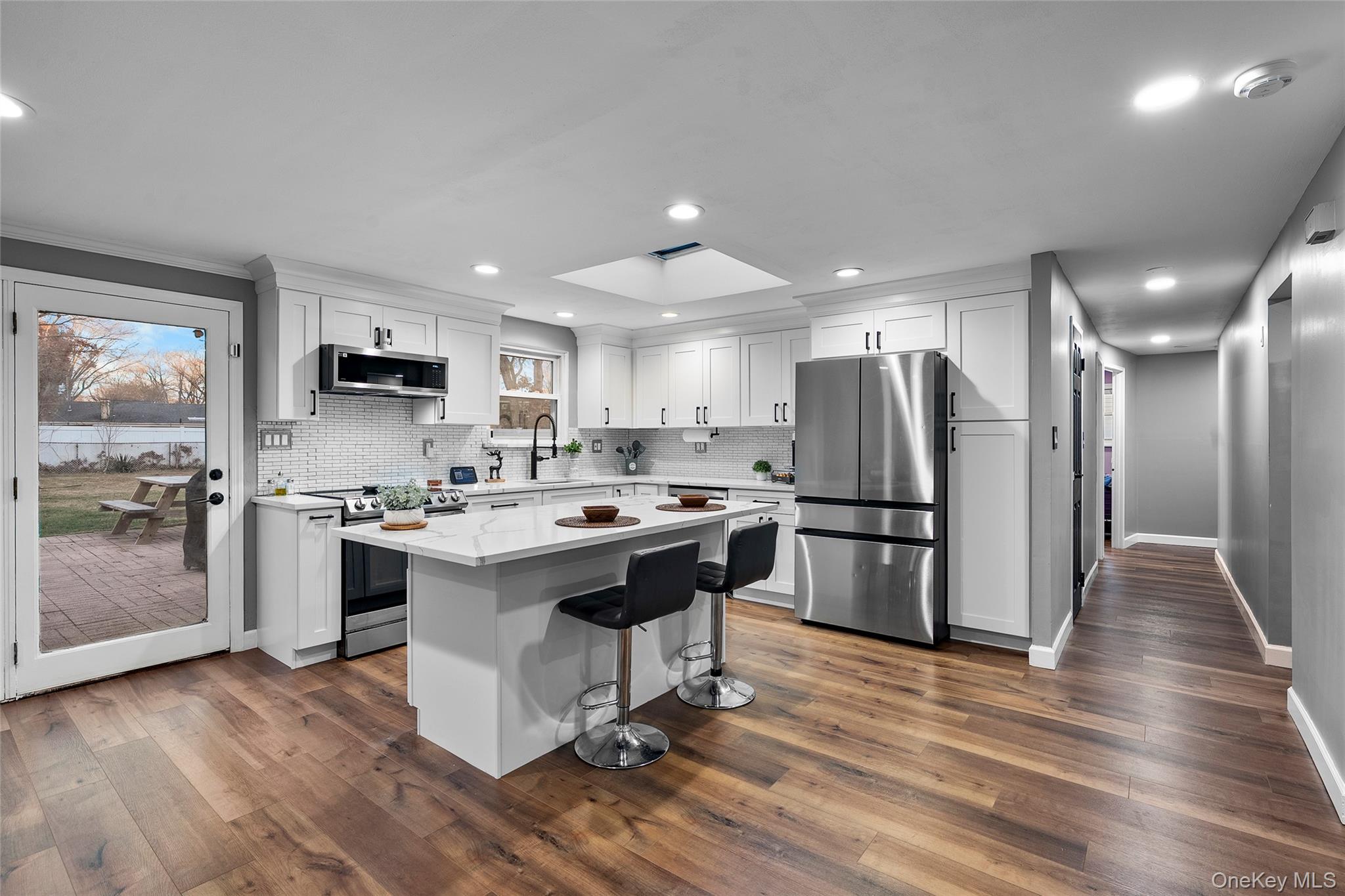 Kitchen featuring a skylight, stainless steel appliances, a kitchen bar, white cabinetry, and dark wood finished floors