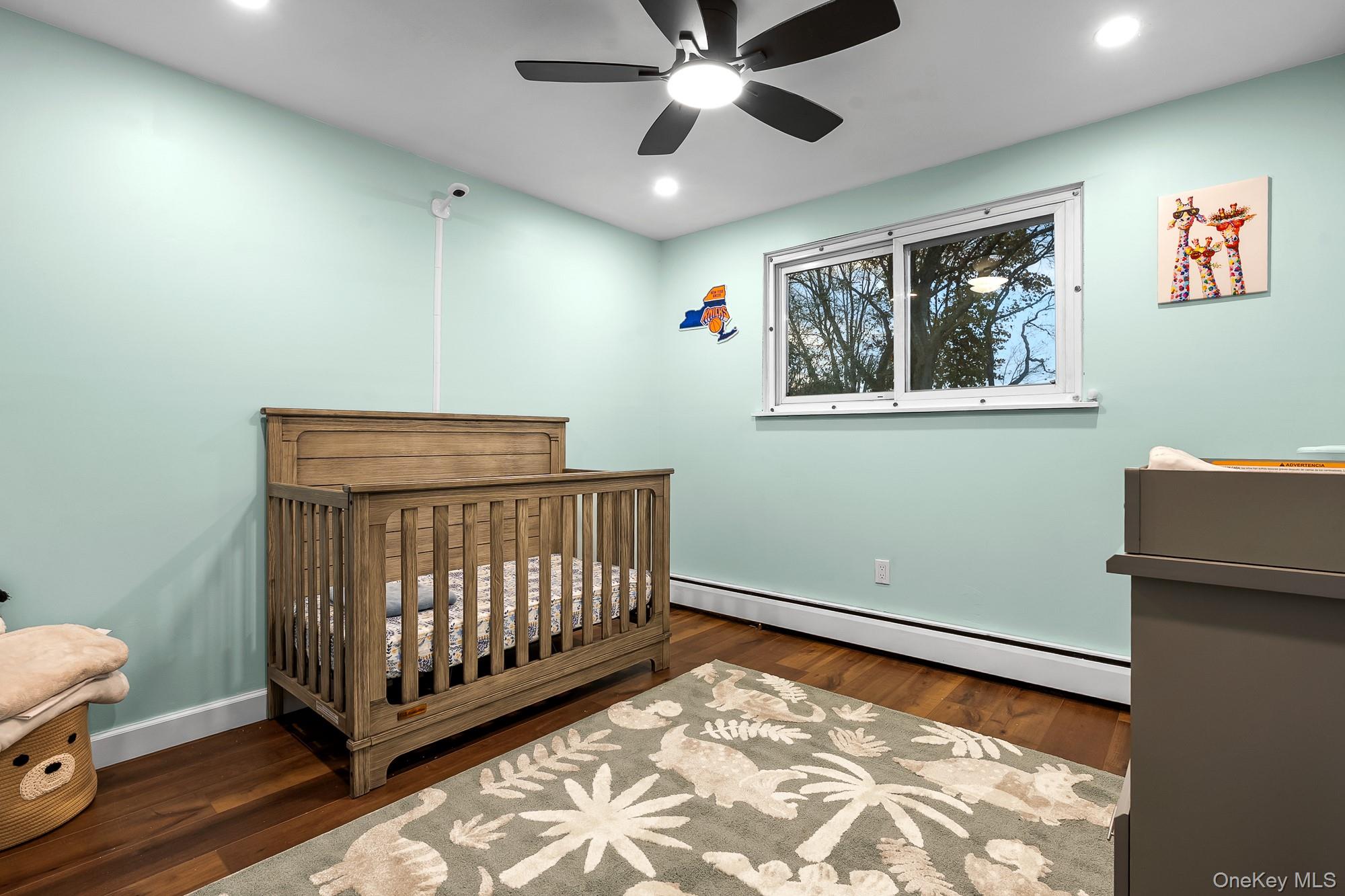 19 Corvette Road Selden, NY 11784 - Photo 17 of 28 Bedroom featuring a baseboard radiator, a nursery area, dark wood-style flooring, recessed lighting, and ceiling fan