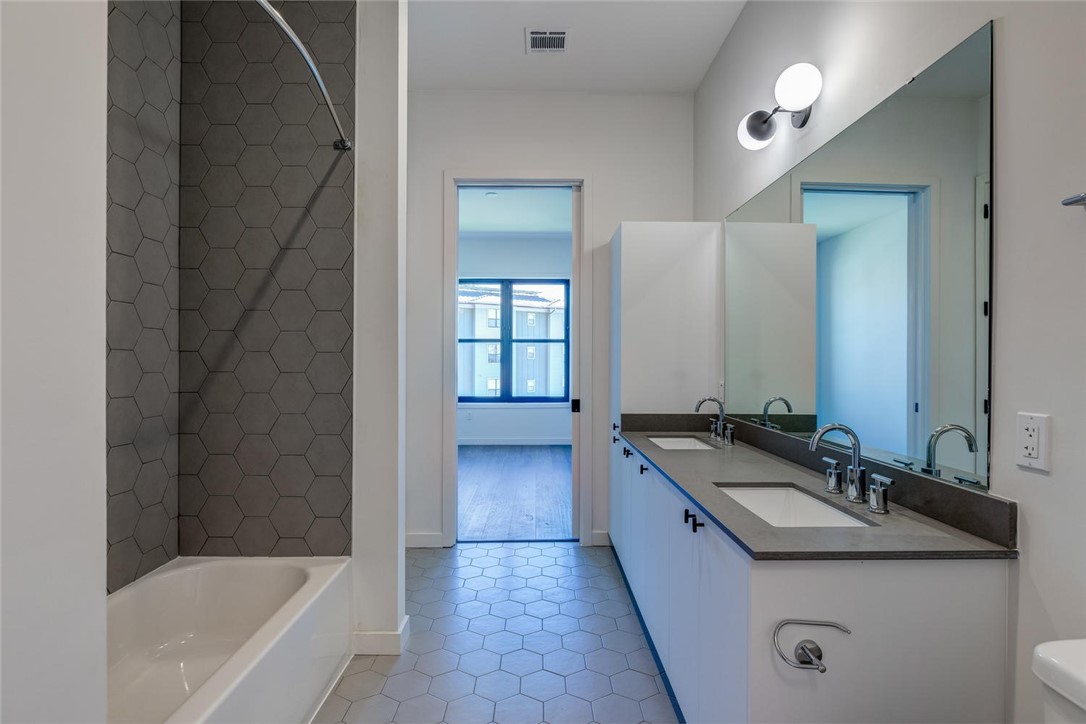 800 Embassy Drive, Unit 233 Austin, TX 78702 - Photo 21 of 40 a bathroom with a granite countertop sink a mirror a bathtub and shower