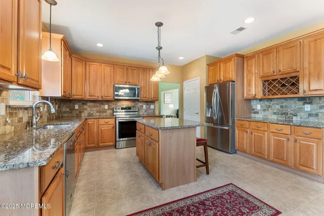 a kitchen with stainless steel appliances granite countertop wooden cabinets a sink a stove a refrigerator and island with wooden floor