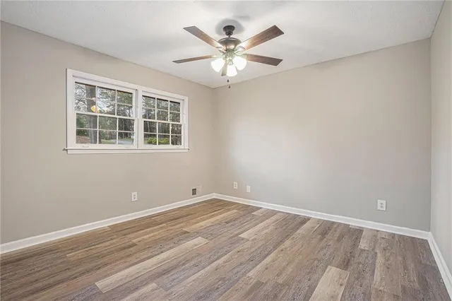 a view of an empty room with wooden floor and a ceiling fan