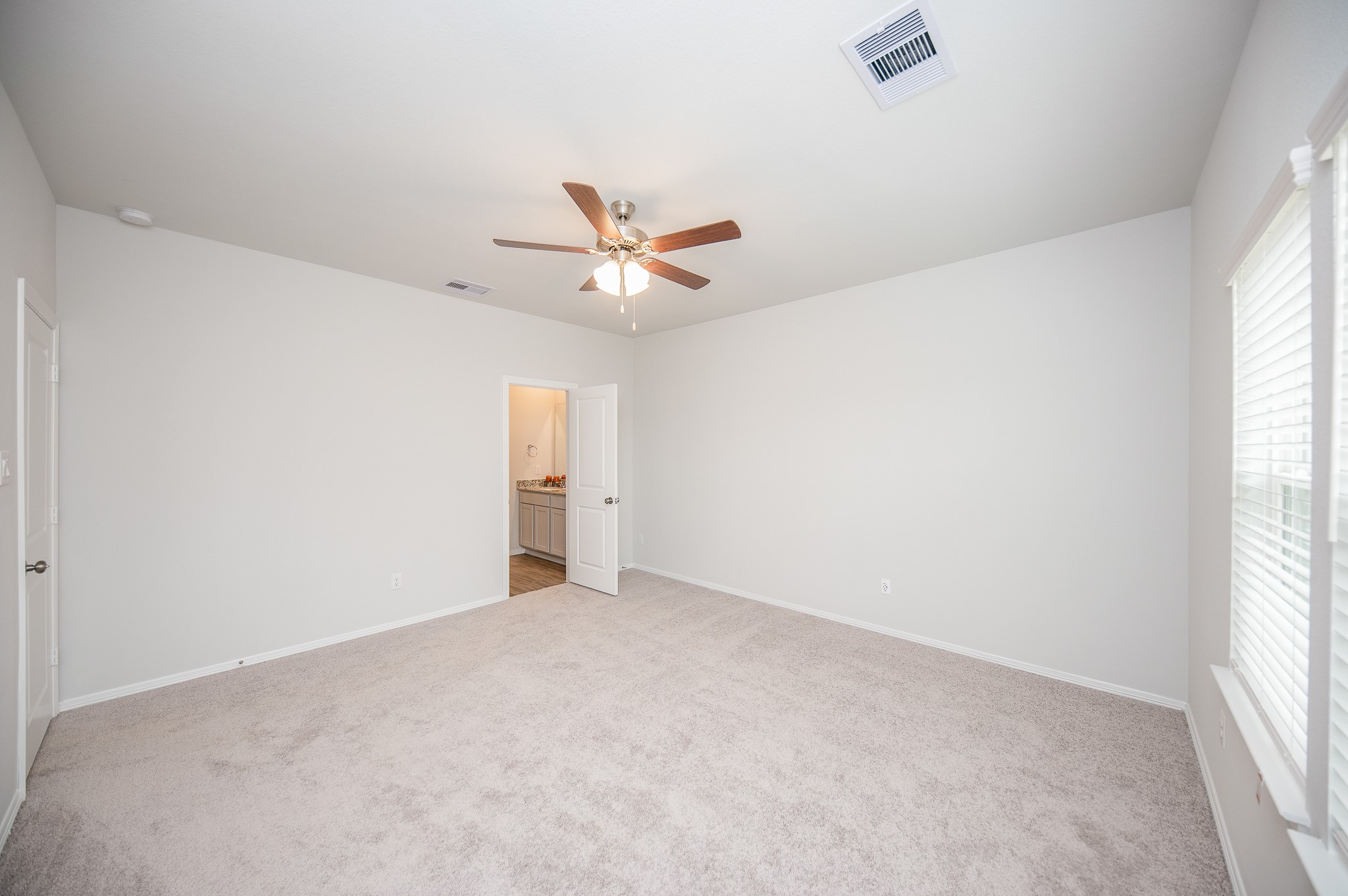 23302 Spring Genesis Lane Katy, TX 77493 - Photo 20 of 32 This spacious bedroom features soft carpet flooring, neutral walls, and a ceiling fan. Natural light streams through the window, and there's an ensuite bathroom for convenience.