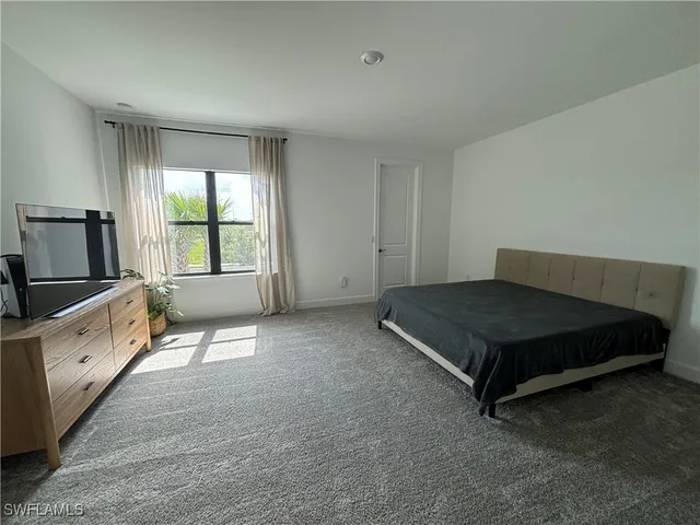 a spacious bedroom with a bed and a flat tv screen on dresser