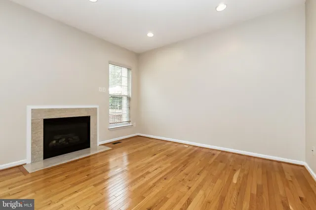 a view of an empty room with wooden floor fireplace and a window