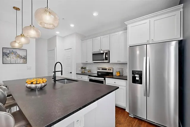 a kitchen with stainless steel appliances granite countertop a refrigerator a stove a sink a dining table and chairs with wooden floor