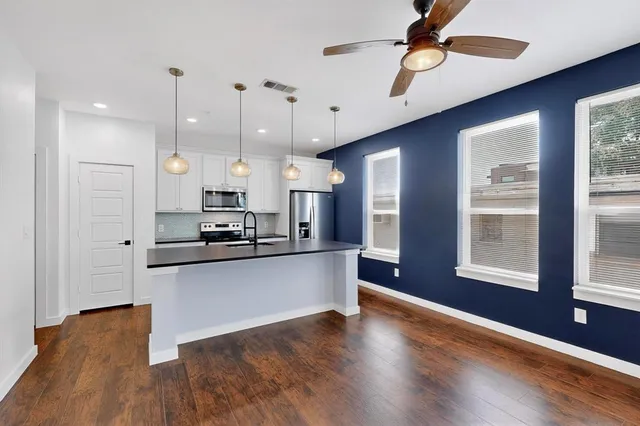 a kitchen with stainless steel appliances kitchen island granite countertop a stove a refrigerator a sink a microwave oven with wooden floor and cabinets