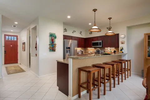 a kitchen with stainless steel appliances kitchen island granite countertop a dining table chairs and a refrigerator