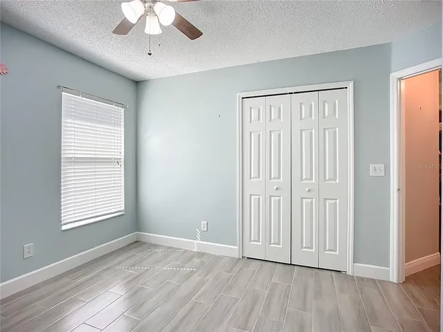 an empty room with wooden floor chandelier fan and windows