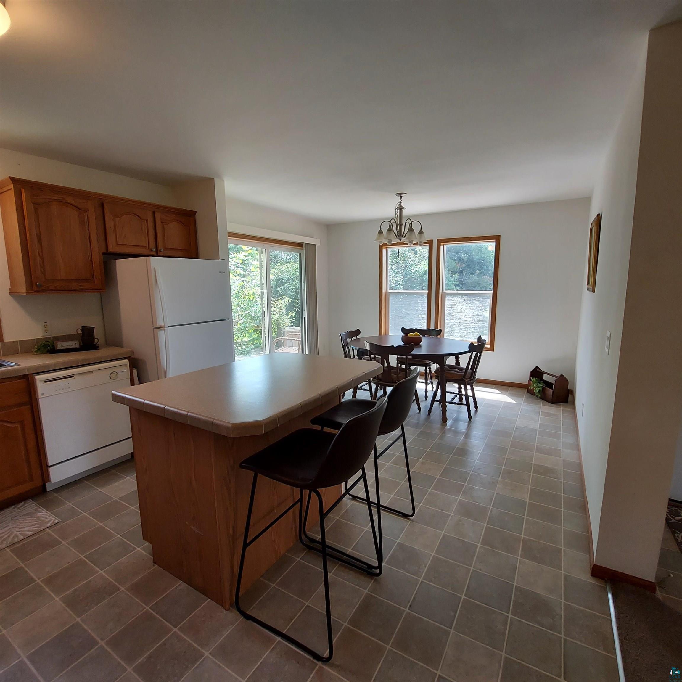 6563 Seville Road Saginaw, MN 55779 - Photo 11 of 28 Kitchen with a notable chandelier, white appliances, a center island, a breakfast bar, and tile patterned flooring